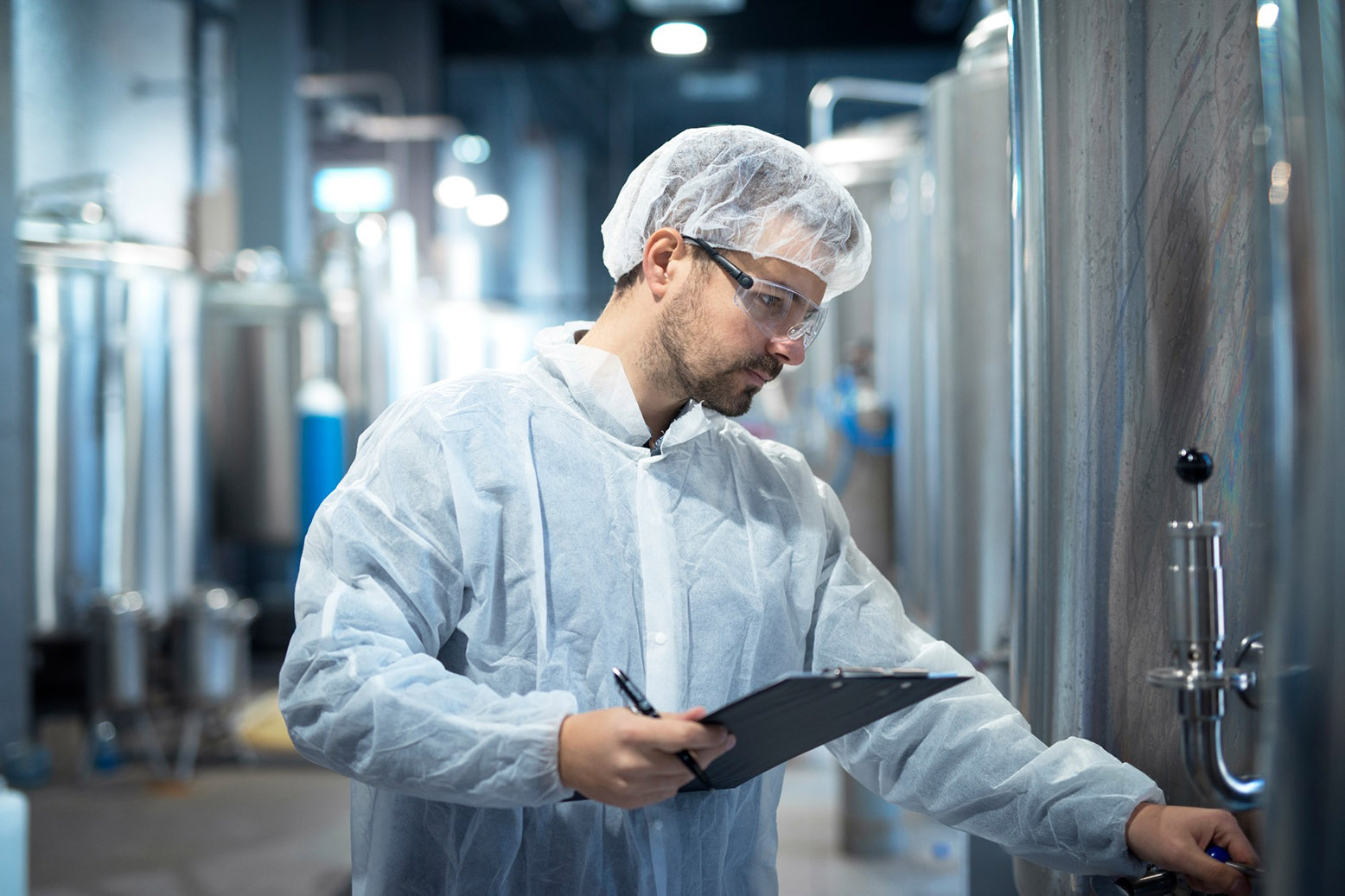 A man dressed in a white coat, hair net and safety classes is running an experiment.